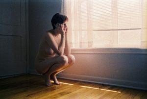 Female model nude, by window, looking out.