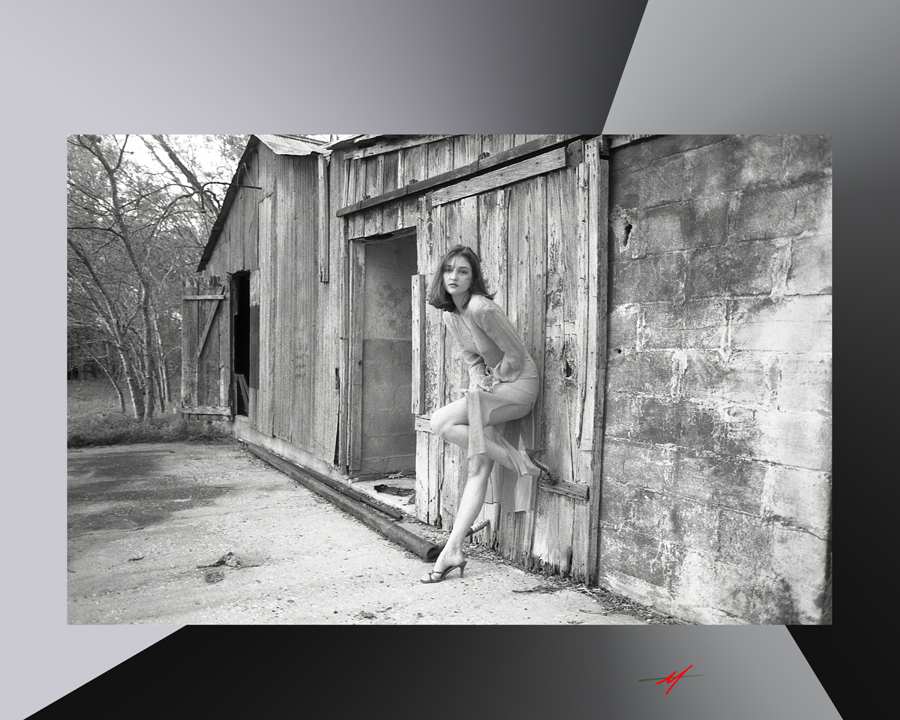Black and white image, red haired female model transparent dress, front of an milk barn.