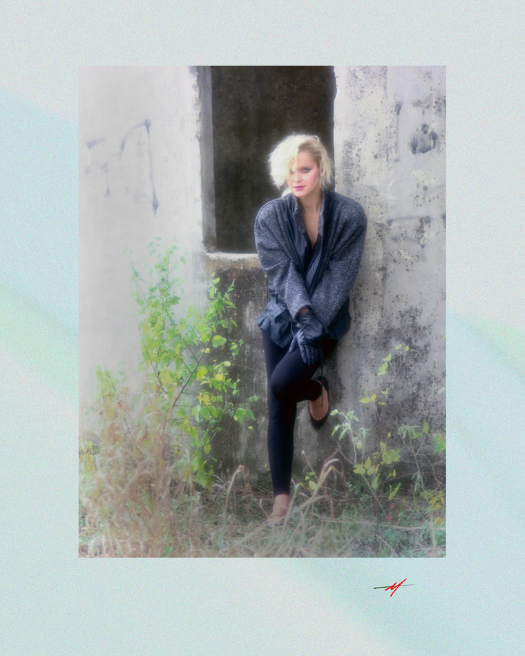 Color image, cute blond, winter wear, standing in front of a silo, last of winter greenery.